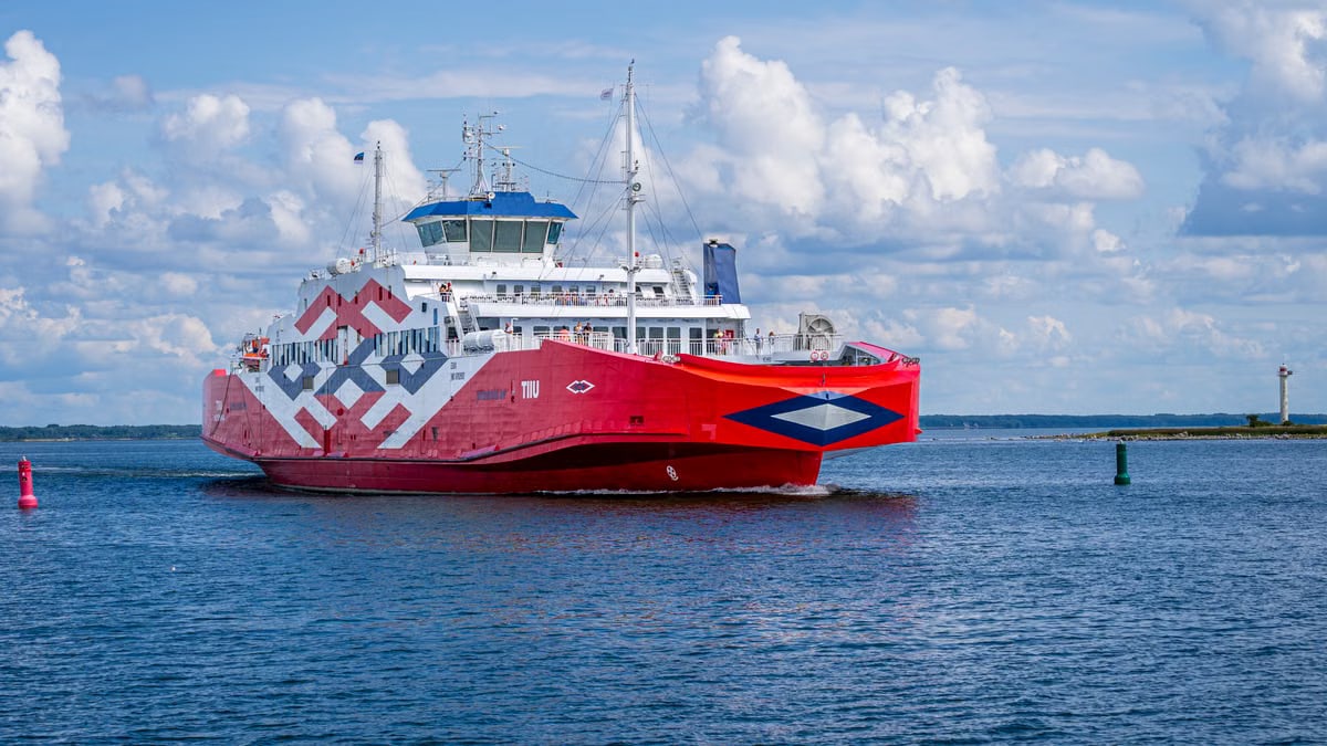 A striking red ferry sails through serene waters in Hiidenmaa, Finland, under a clear blue sky.